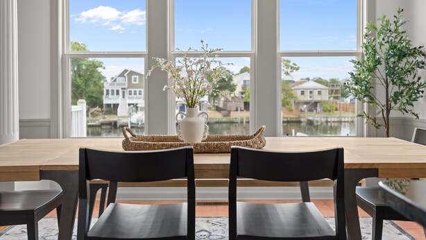 Ein Essbereich mit einem Holztisch, schwarzen Stühlen, einer gewebten Tischmatte und einer weißen Vase mit Blumen.