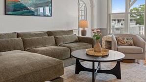 Ein Wohnzimmer mit einer Eckcouch, einem runden Couchtisch, einem Beistelltisch mit Lampe und einem Sessel mit gemustertem Kissen.