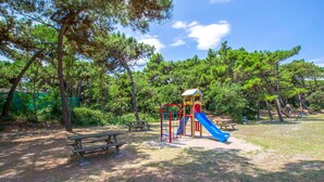 Ein Spielplatz mit Rutsche und Klettergeräten, umgeben von Bäumen und Picknicktischen.