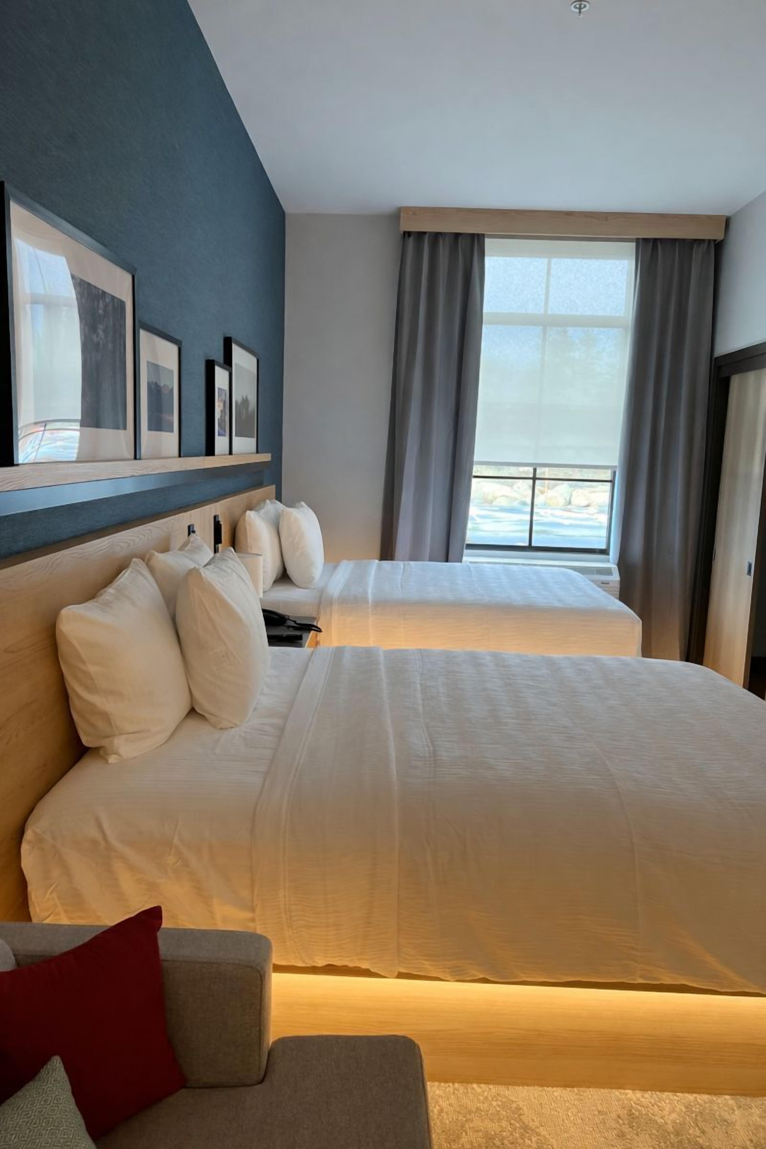 A hotel room with two beds, a large window with curtains, and framed pictures on the wall.
