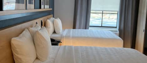 A hotel room with two beds, a large window with curtains, and framed pictures on the wall.