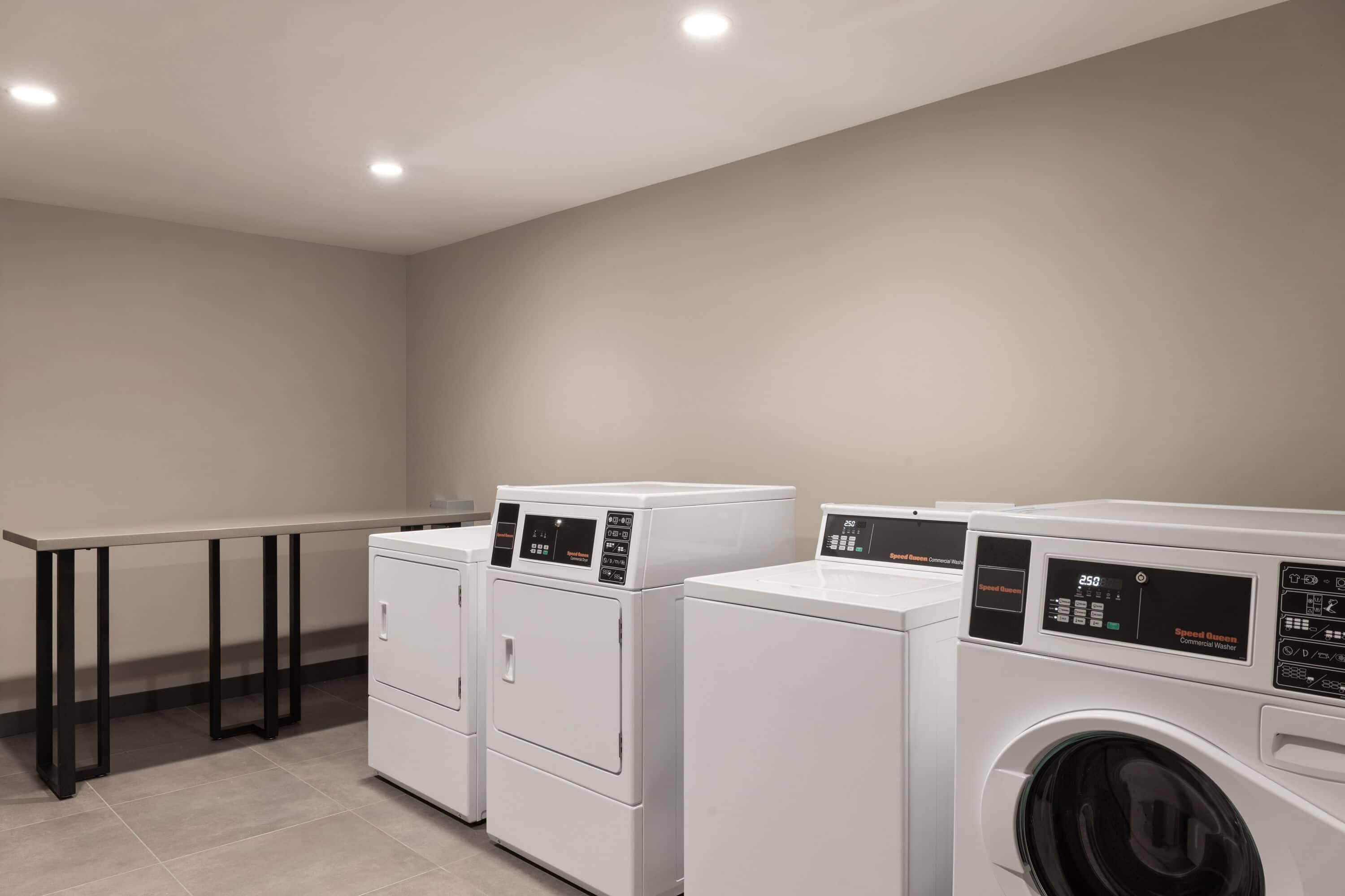 A laundry room with three white washing machines, a table, and black metal legs.