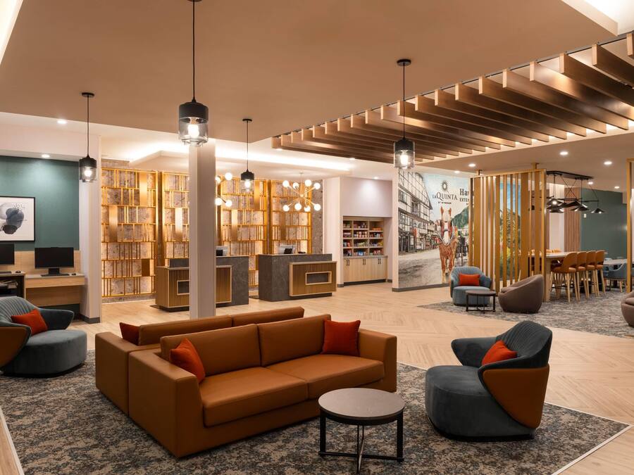 A modern hotel lobby with a sofa, armchairs, a reception desk, and a library.