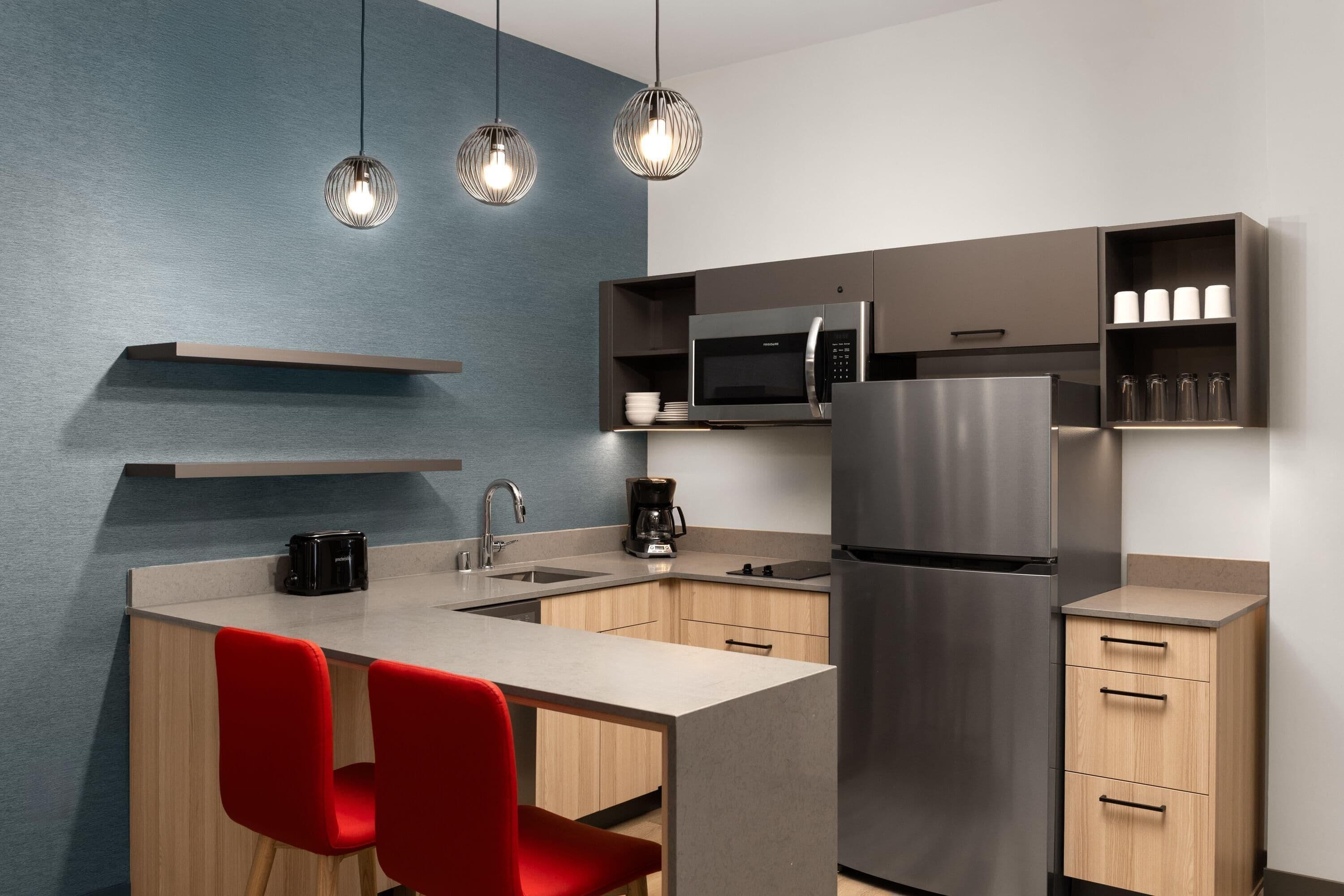 A modern kitchen with a central island, stainless steel appliances, and red chairs.
