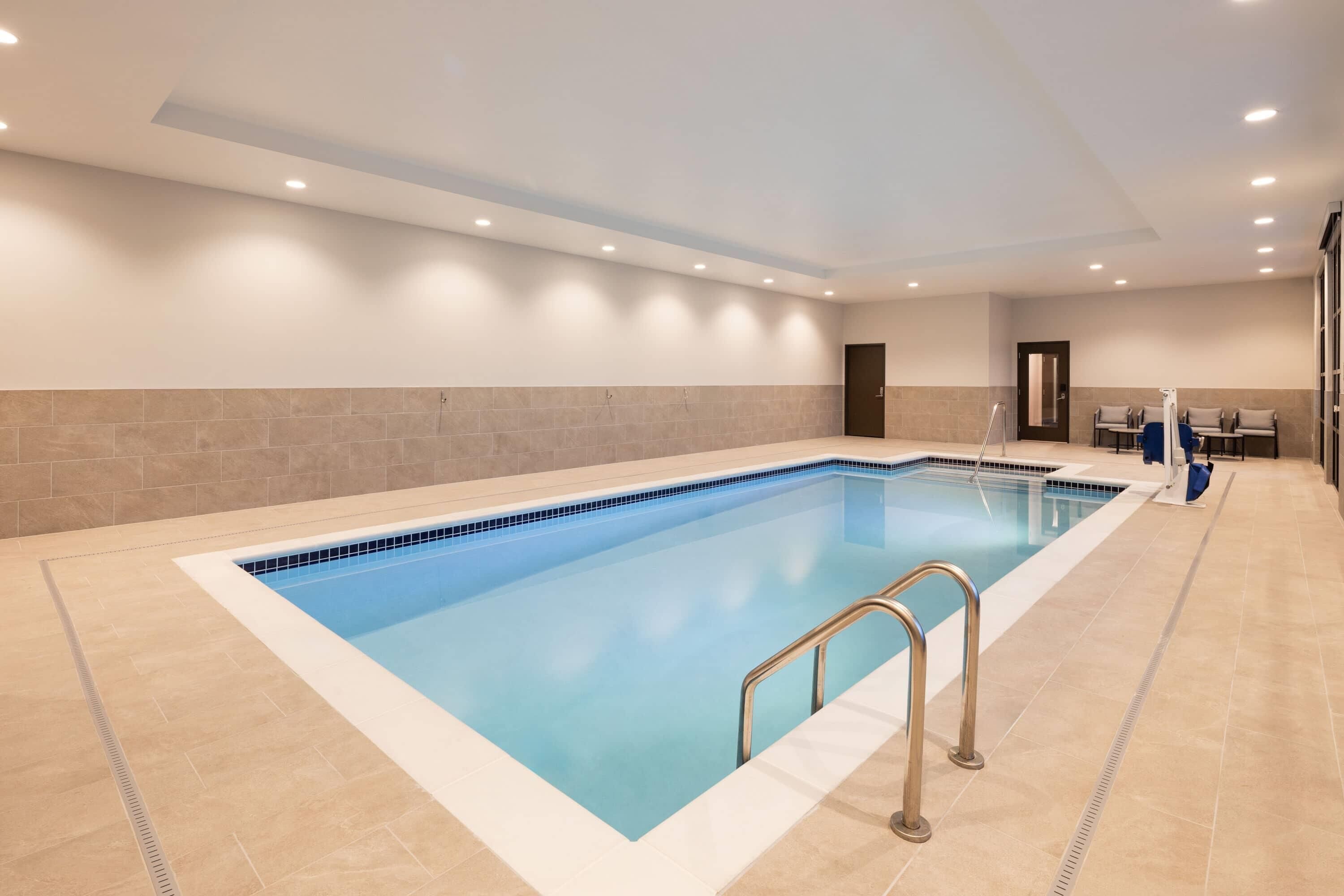 A swimming pool with a tiled deck, a metal ladder, and a door in the background.