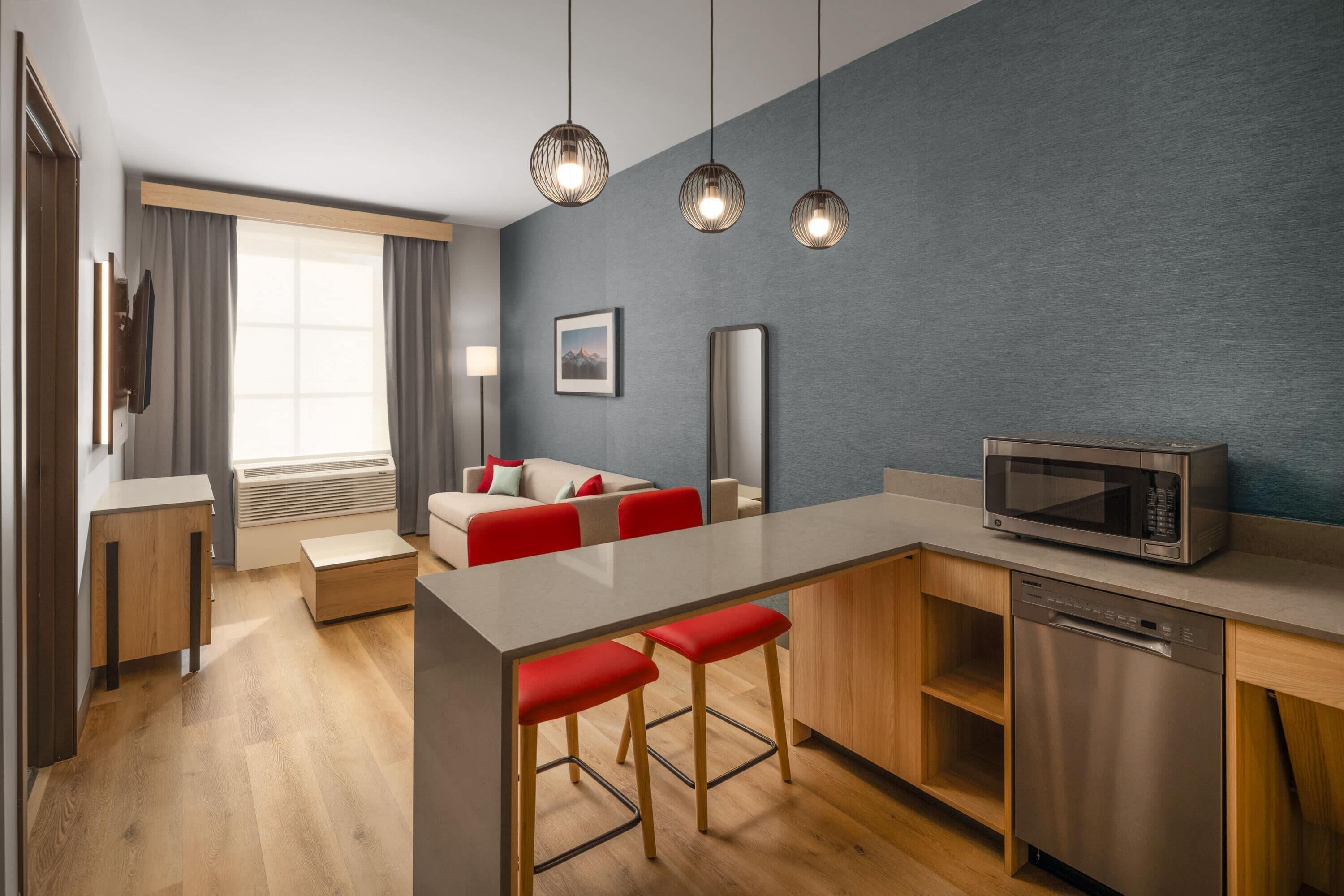 A modern kitchen with a central island, bar stools, a microwave, and a dishwasher.