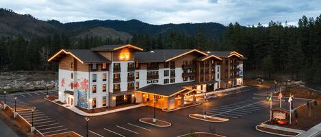 A multi-story hotel with a central courtyard, parking lot, and a mountainous backdrop.