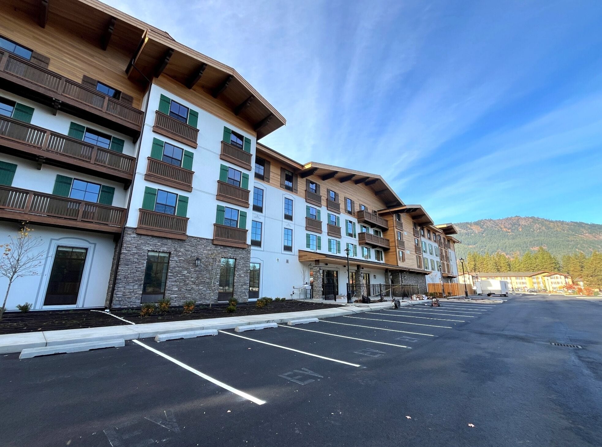 A multi-story hotel with balconies, a parking lot, and a mountainous backdrop.