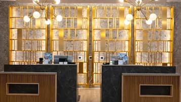 Un espace d’accueil comprenant deux comptoirs de réception, un panneau de signalisation numérique indiquant les sorties et un mur décoratif orné d’un motif géométrique.