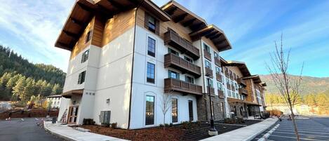 A multi-story building with balconies, a parking lot, and a mountainous backdrop.