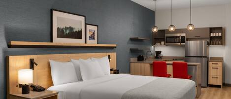 Une chambre d’hôtel comprenant un lit, une table de chevet, une lampe et un coin cuisine équipé d’un four à micro-ondes, d’un réfrigérateur et de chaises rouges.