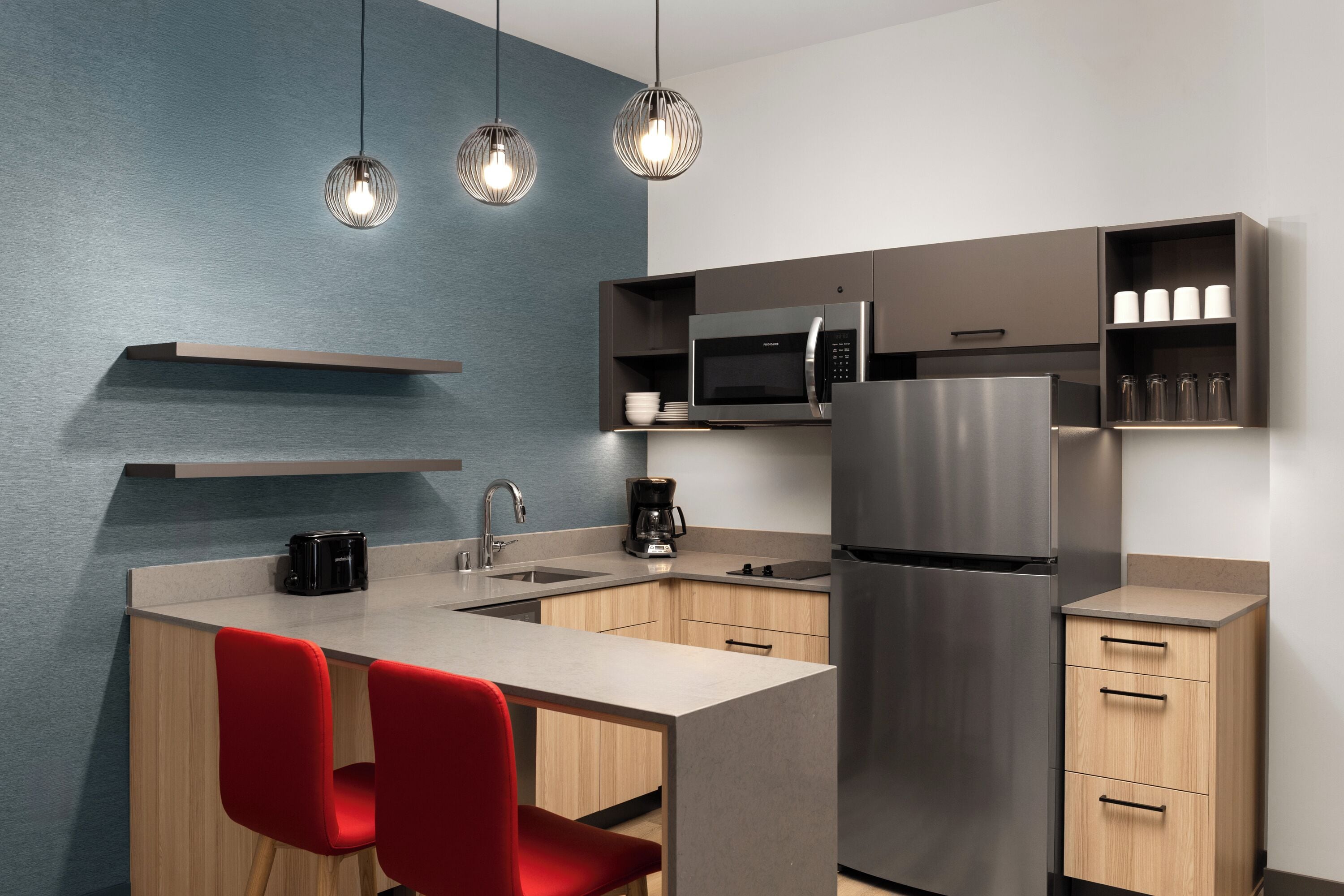 A modern kitchen with a central island, stainless steel appliances, and red chairs.