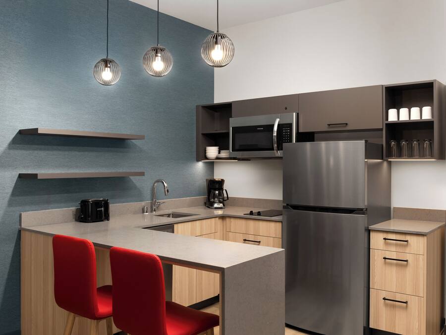 A modern kitchen with a central island, stainless steel appliances, and red chairs.
