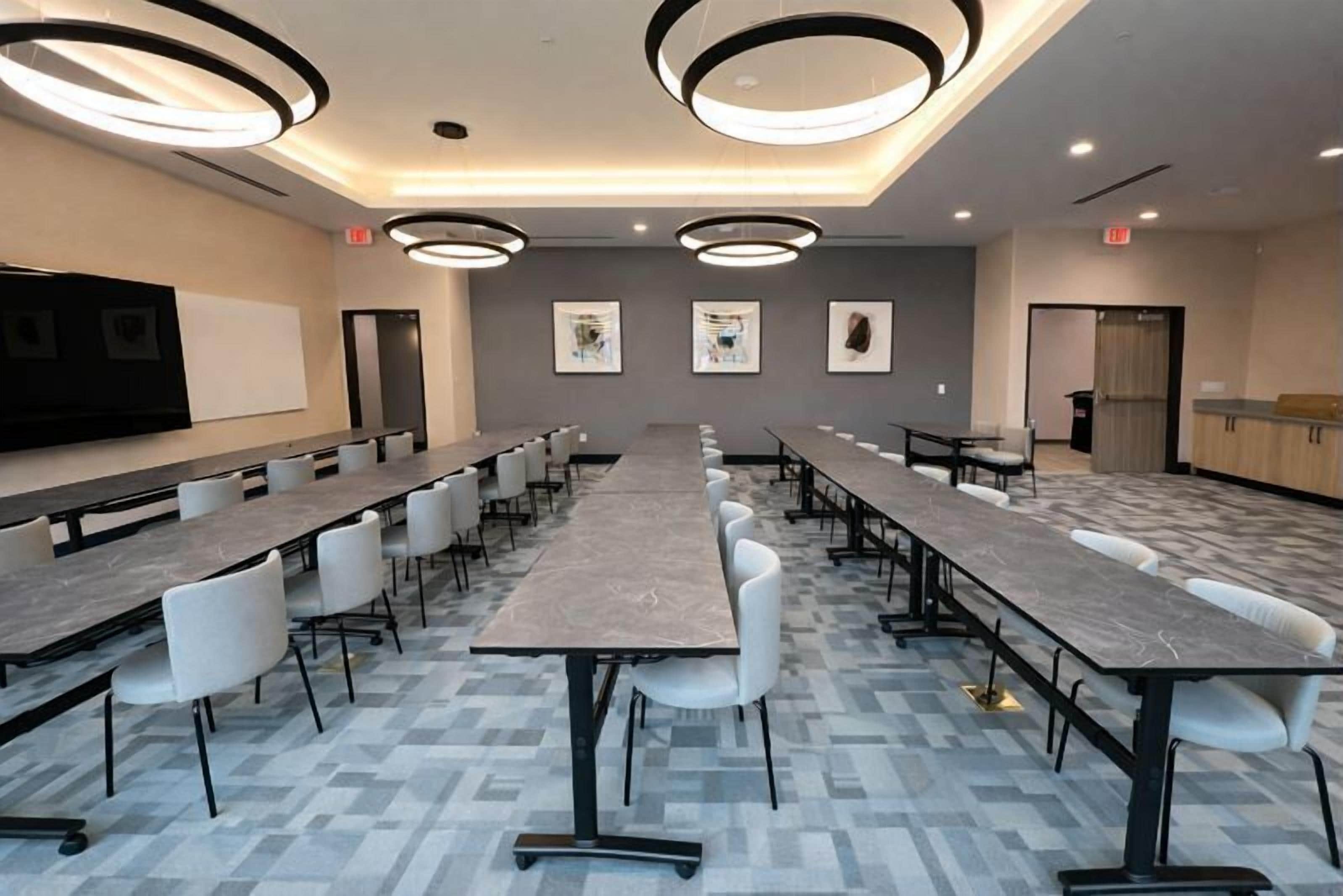 Une salle de conférence avec de longues tables et des chaises, un tableau blanc et des œuvres d’art encadrées accrochées aux murs.