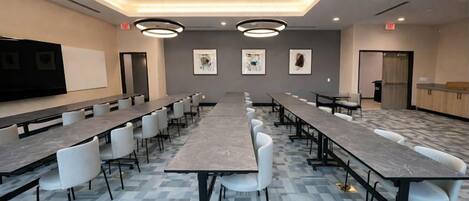 Une salle de conférence avec de longues tables et des chaises, un tableau blanc et des œuvres d’art encadrées accrochées aux murs.