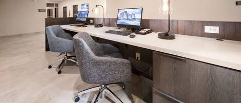A reception desk with two computer monitors, a telephone, and a lamp. There are two office chairs and a trash bin.
