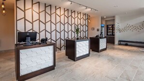 Ein Empfangsbereich mit drei Schreibtischen, einer Wand mit geometrischen Mustern und einer Pflanze.