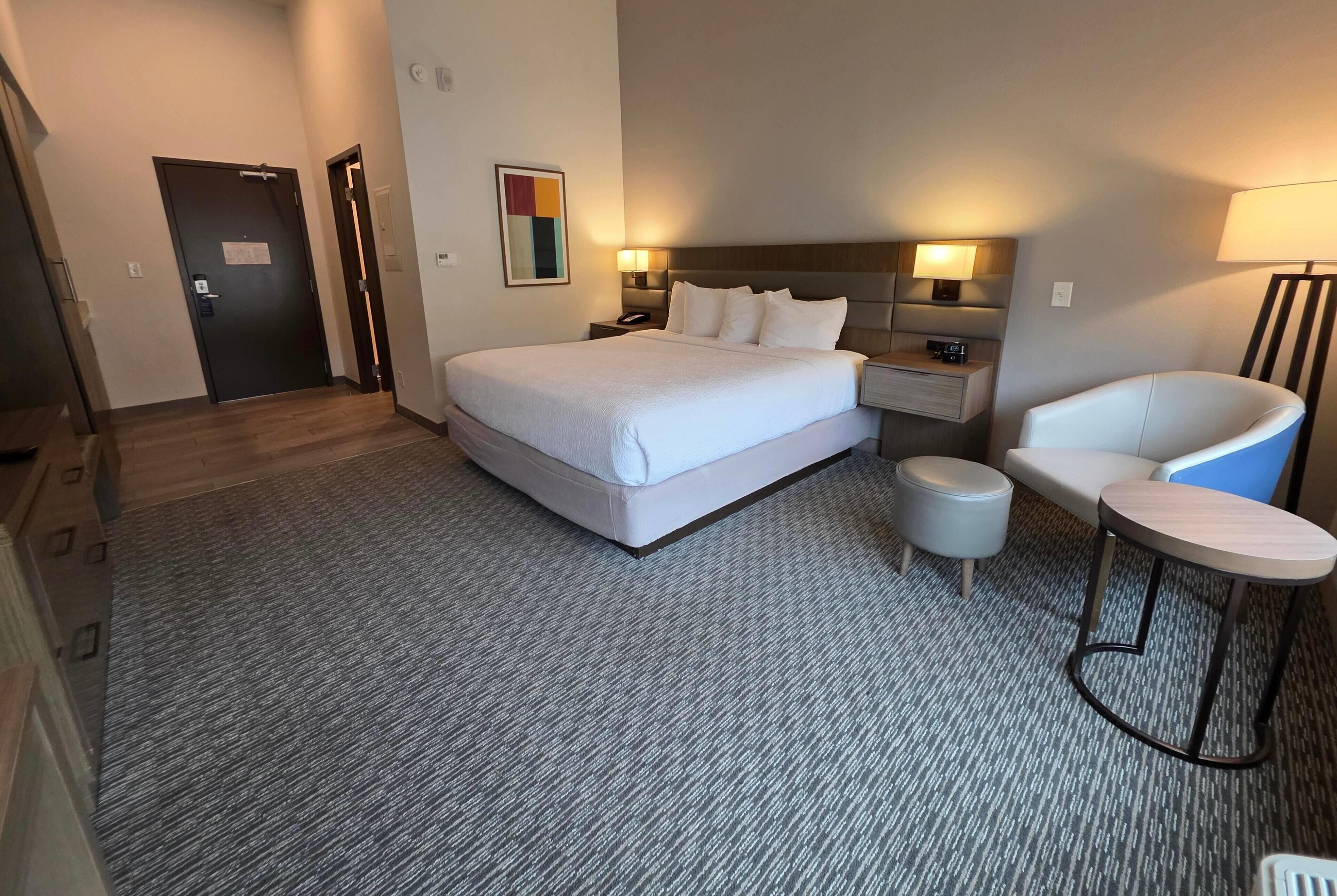A hotel room with a large bed, a desk, a chair, and a small table.