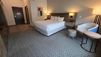 A hotel room with a large bed, a desk, a chair, and a small table.