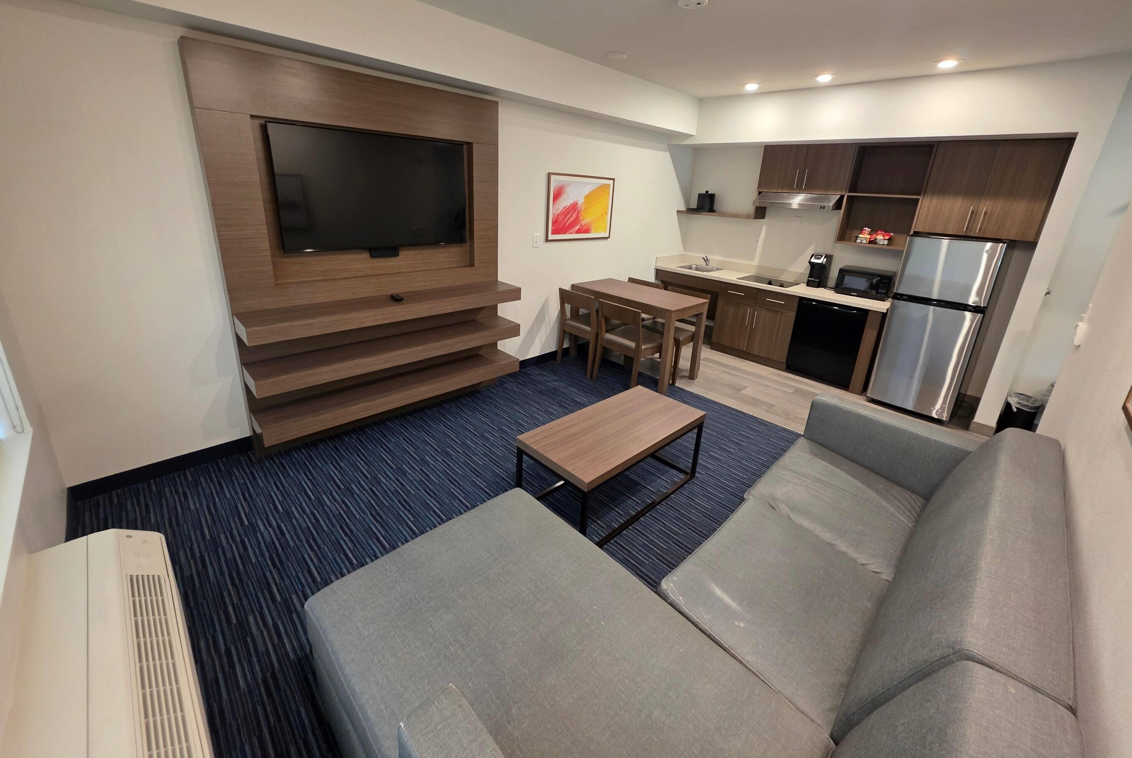 A modern living room with a flat-screen TV, a sofa, a coffee table, and a dining area with a small table and chairs.