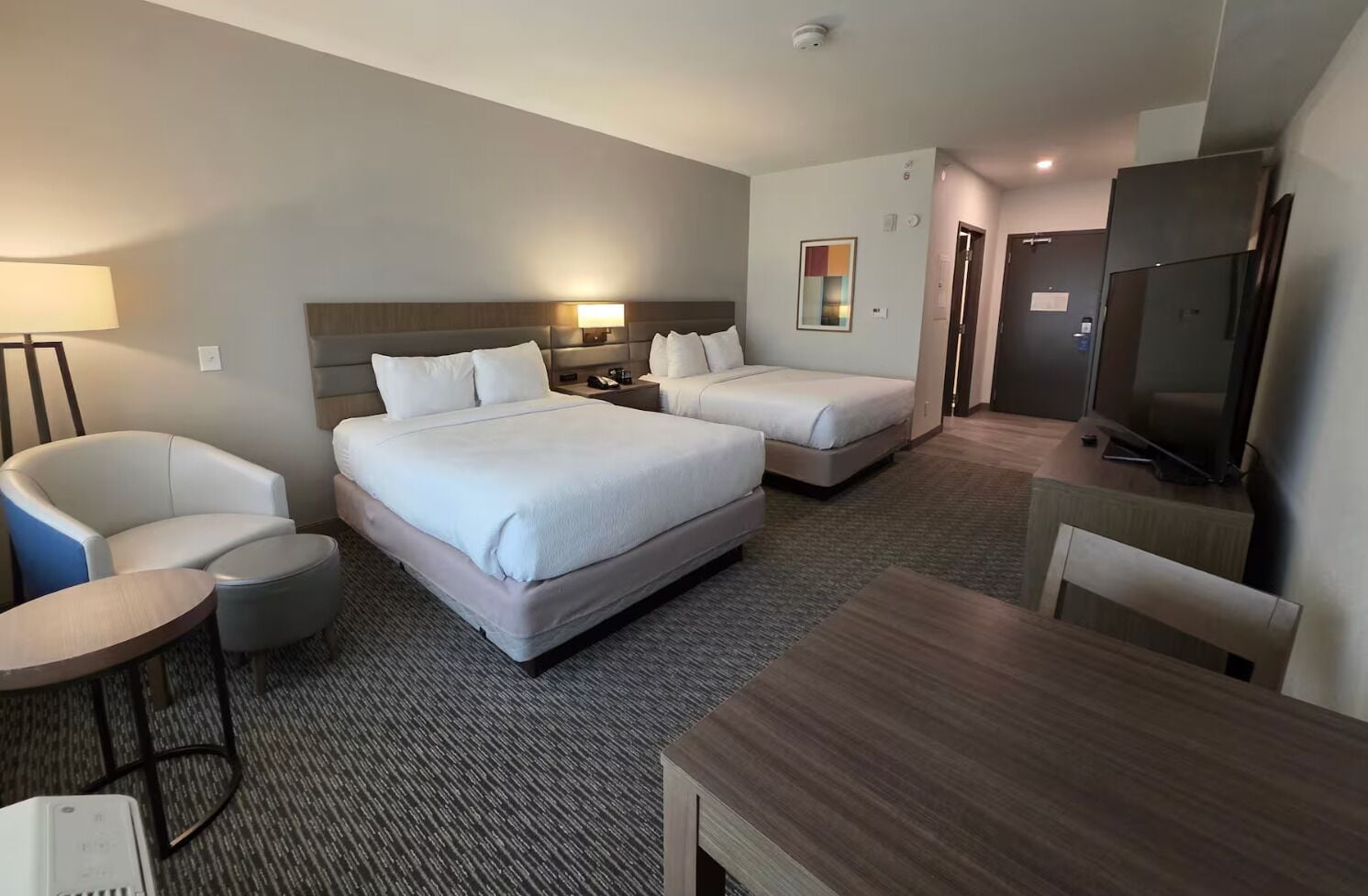 Une chambre d’hôtel avec deux lits, un bureau, une chaise, une télévision et une lampe.