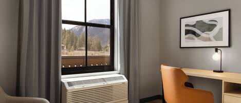 A room with a large window, a desk, an orange office chair, a white radiator, and a framed picture on the wall.