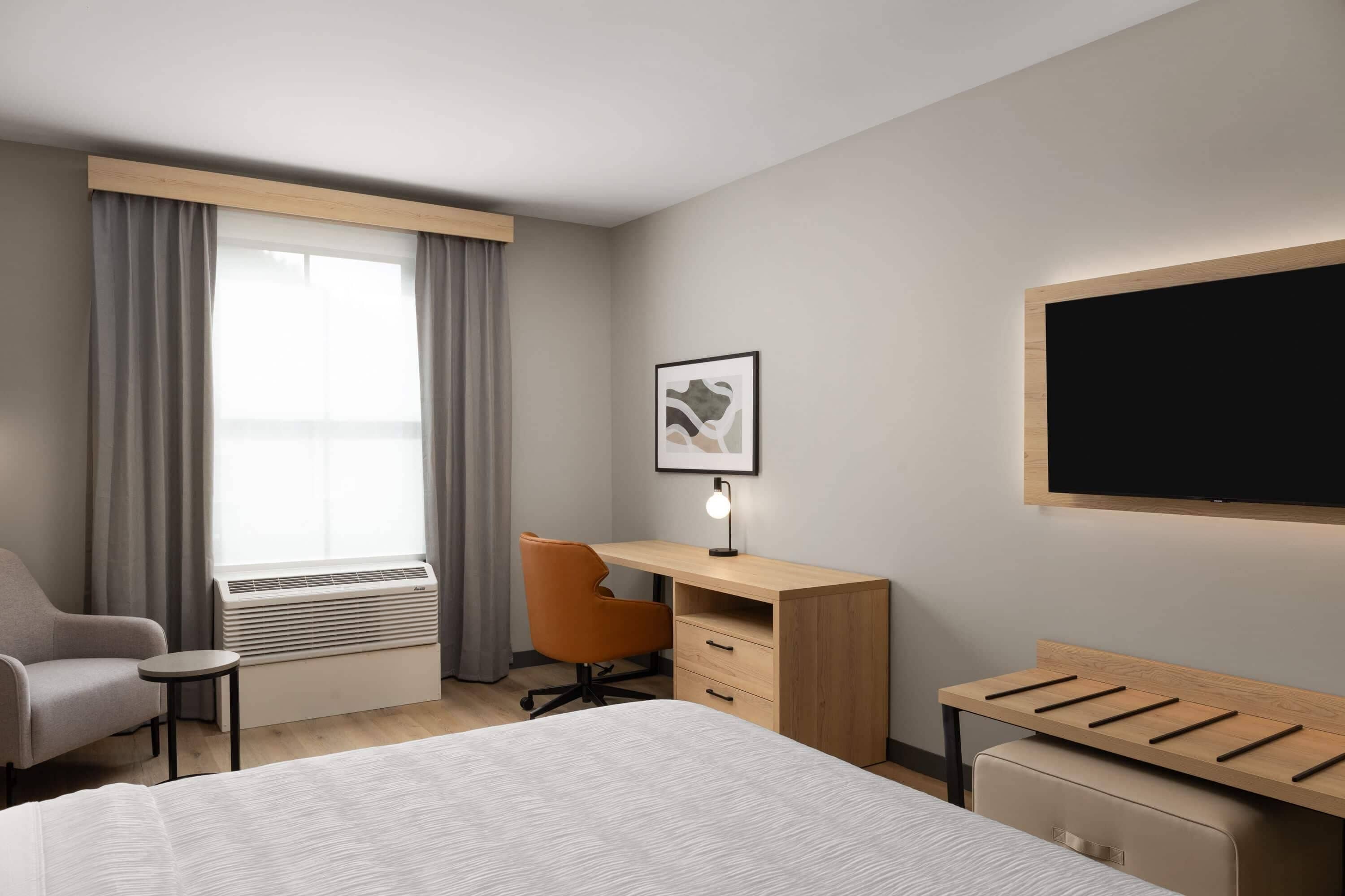 Une chambre d’hôtel avec un lit, un bureau, une chaise, une télévision et une fenêtre avec des rideaux.