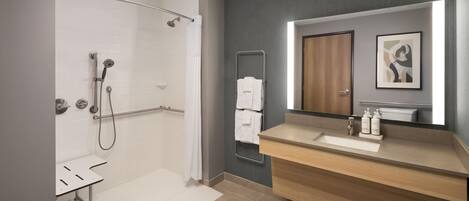 Un baño moderno con ducha, lavamanos, espejo y perchero.