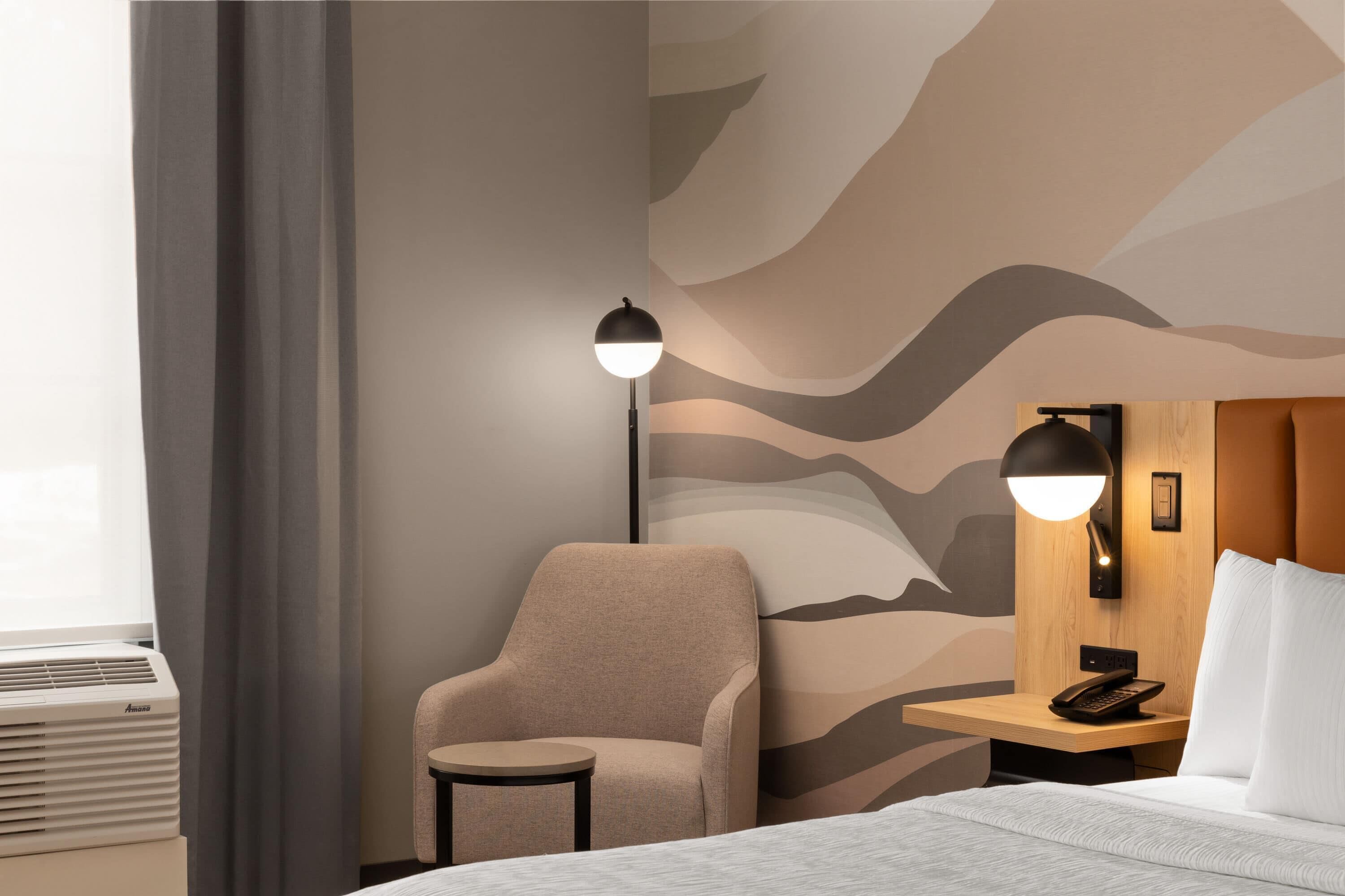 Een hotelkamer met een bed, een stoel, een klein tafeltje, een telefoon aan de muur en een muur met een golvend patroon.