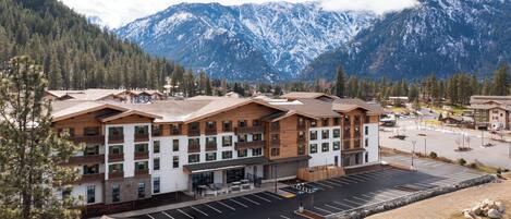 A multi-story hotel with a parking lot, surrounded by mountains and trees.