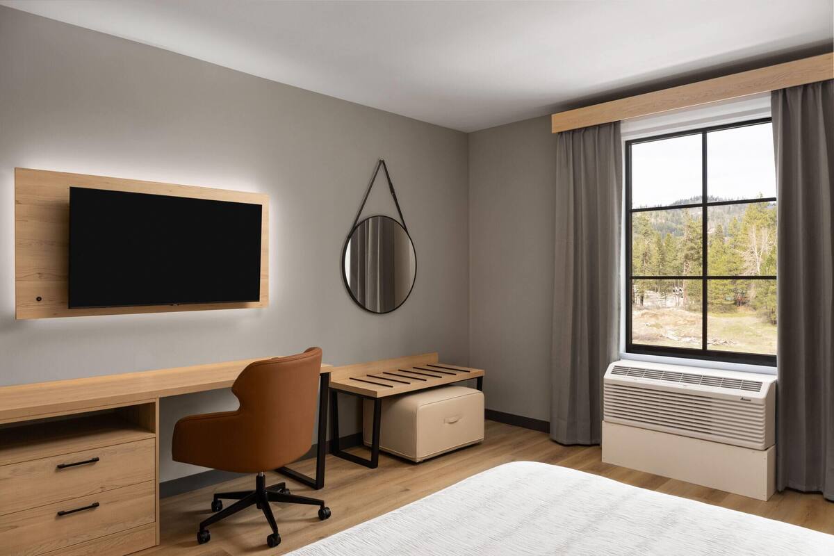 Habitació d'hotel moderna amb escriptori de fusta, cadira còmoda, televisió de pantalla plana, mirall rodó, finestra amb cortines i aire condicionat integrat.