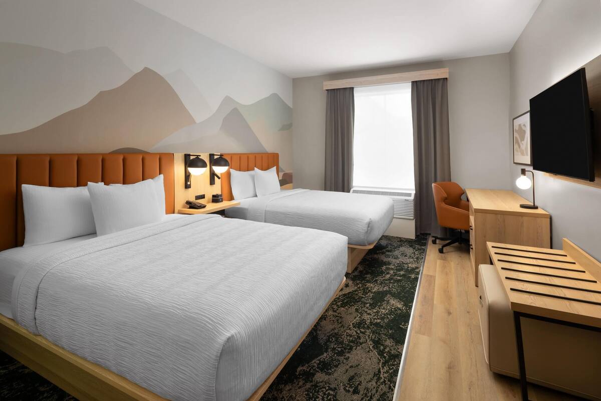Habitació d'hotel amb dos llits, una taula, una cadira, un televisor i una finestra amb cortines.
