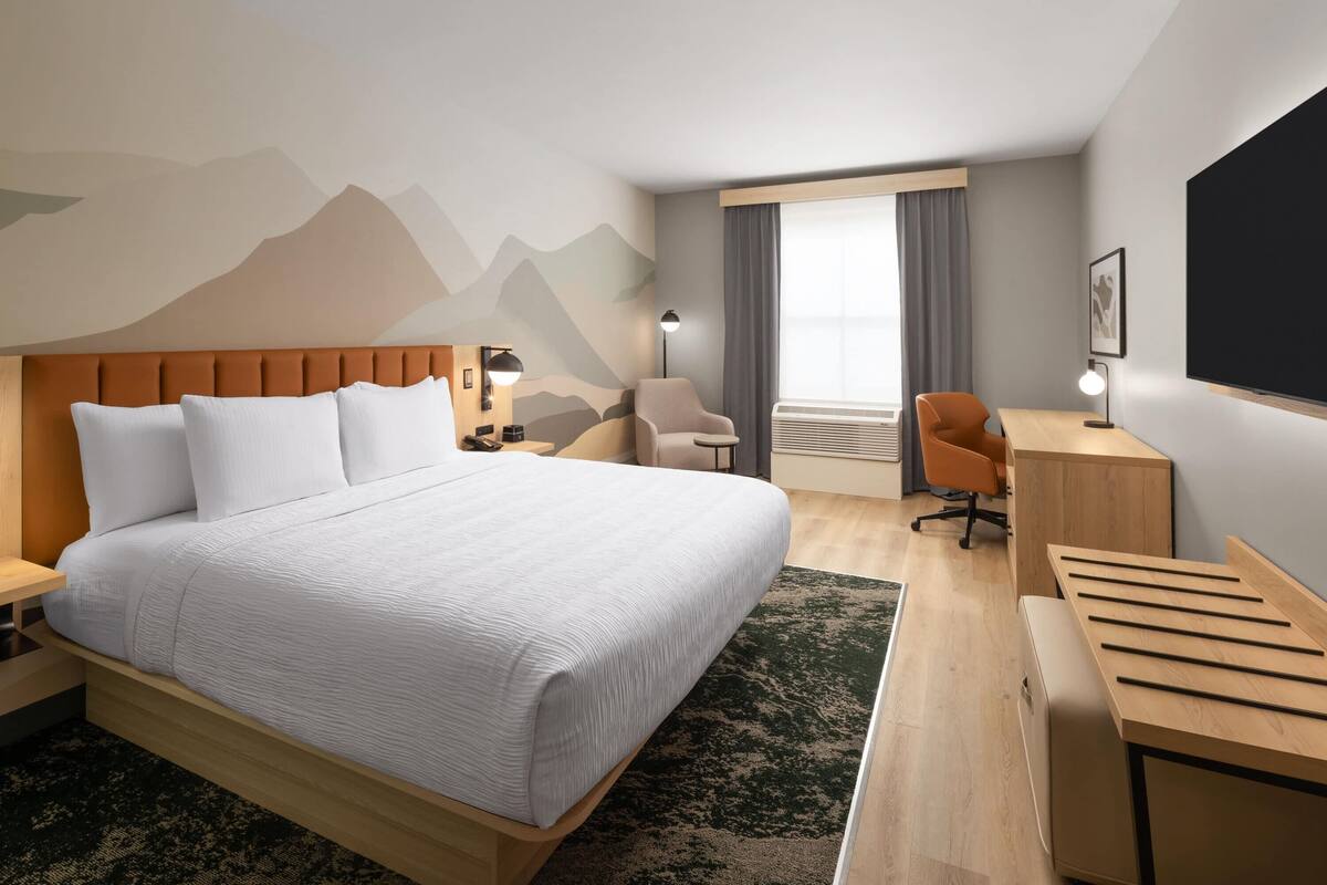 Habitació d'hotel amb un llit gran, una taula de treball, una cadira, un televisor i una finestra amb cortines.