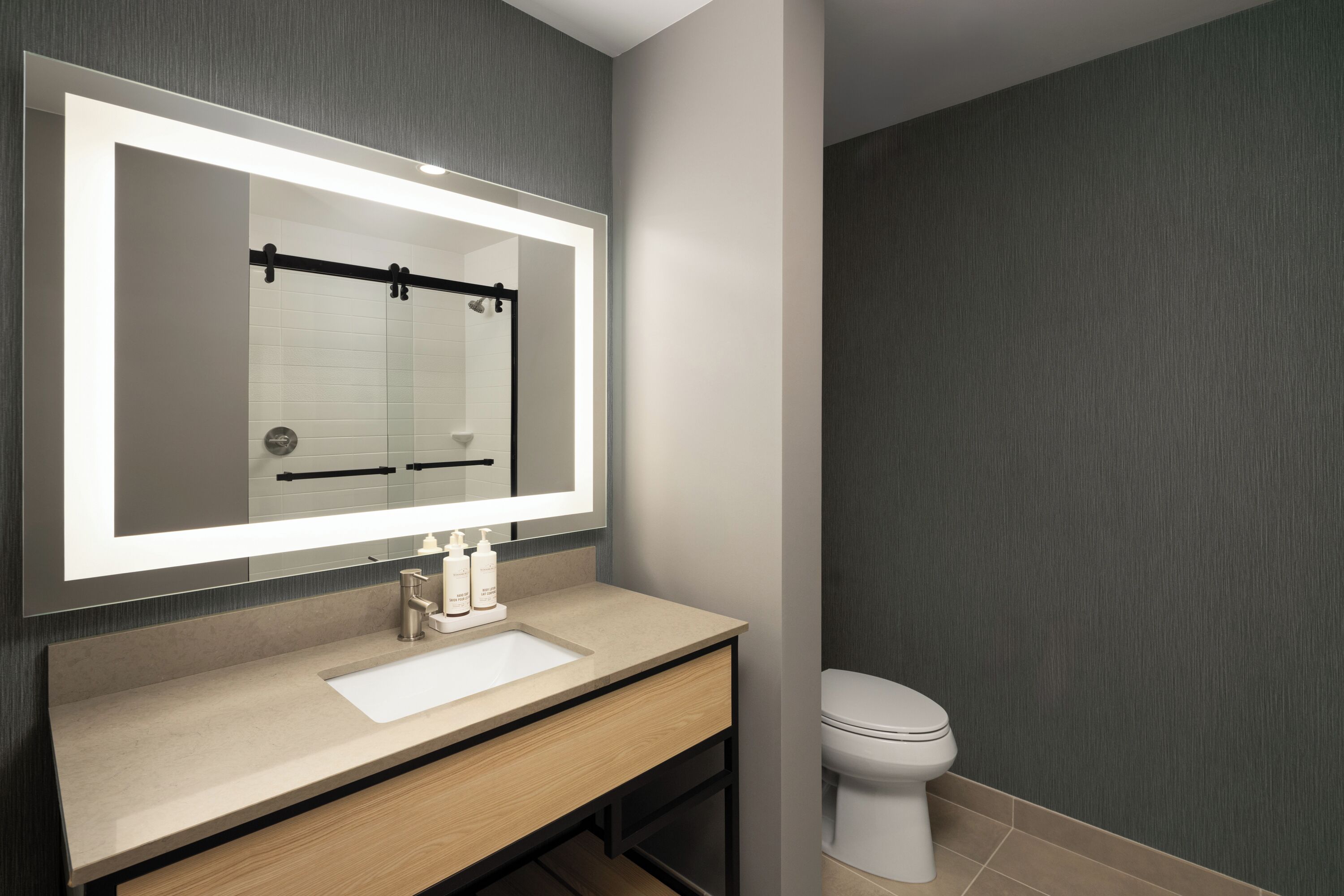 Un baño moderno con un espejo grande, un lavamanos y un inodoro.