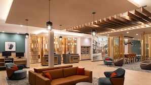 Een moderne hotellobby met een bank, fauteuils, een receptiebalie en een bibliotheek.