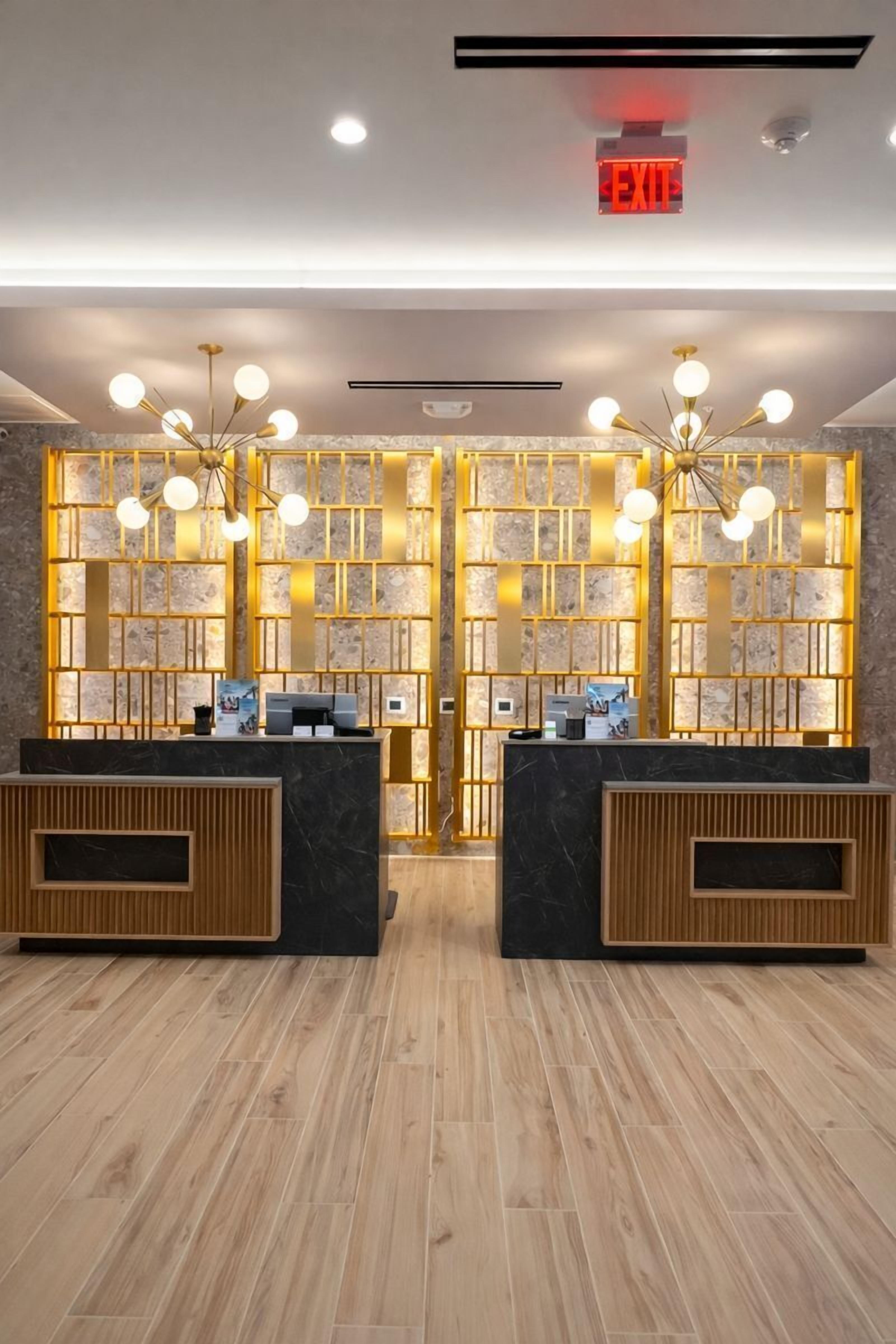 Zona de recepción con dos mostradores, un letrero de salida digital y una pared decorativa con diseño geométrico.