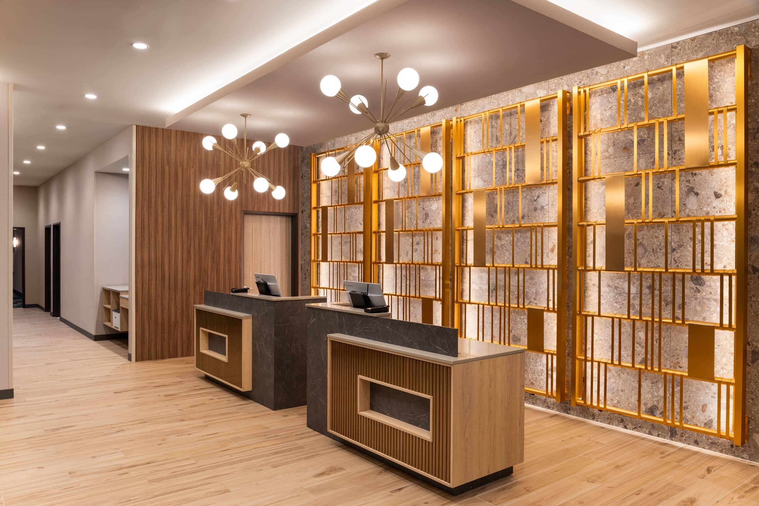 A reception area with wooden reception desks, a modern chandelier, and a stone wall with a geometric pattern.
