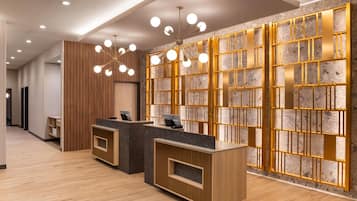A reception area with wooden reception desks, a modern chandelier, and a stone wall with a geometric pattern.
