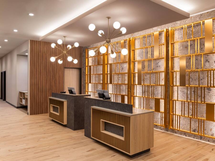 A reception area with wooden reception desks, a modern chandelier, and a stone wall with a geometric pattern.