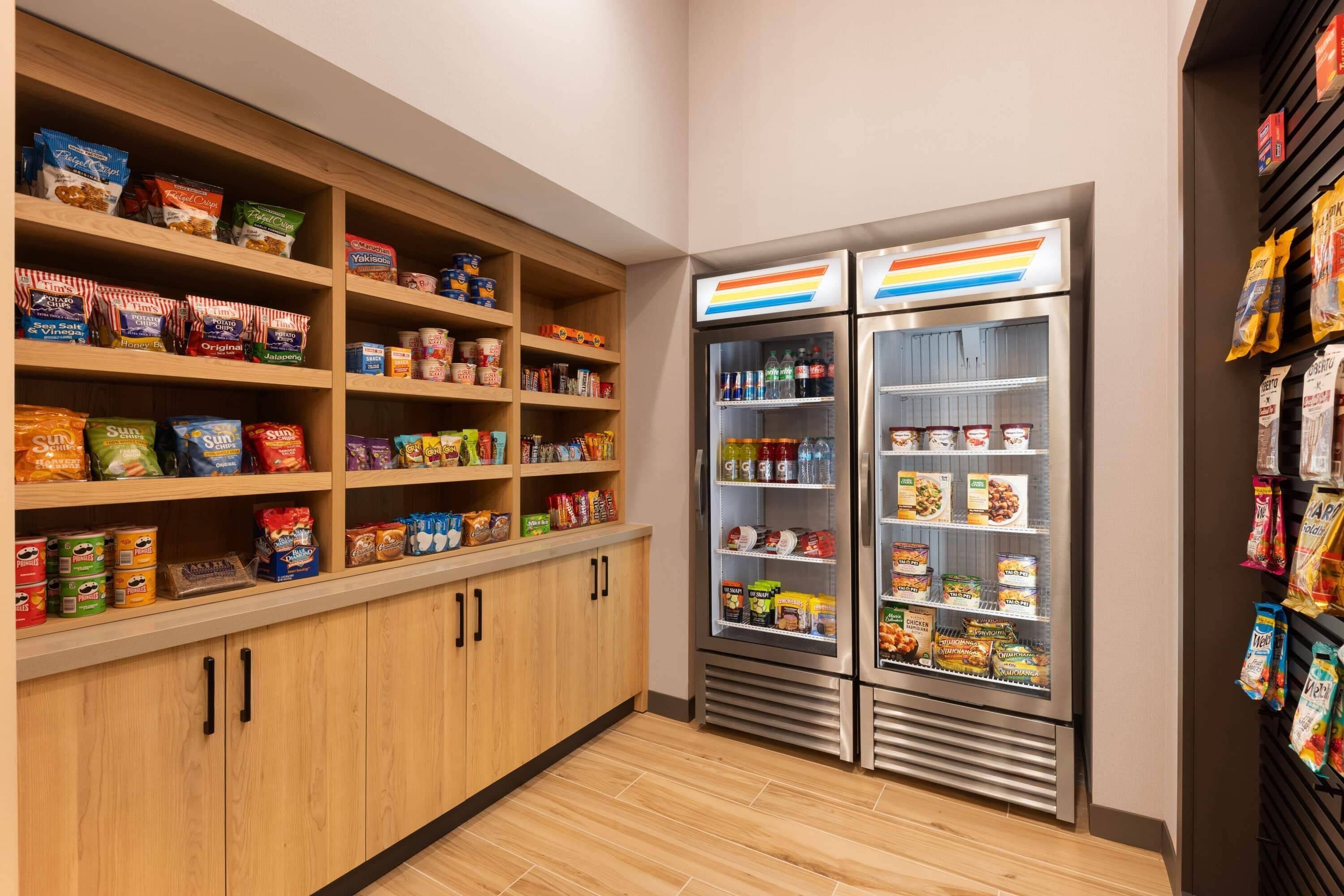 A pantry with shelves stocked with snacks and a refrigerator with beverages.