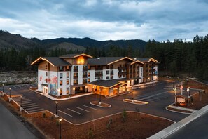 Un hotel a più piani con cortile interno, parcheggio e montagne sullo sfondo.