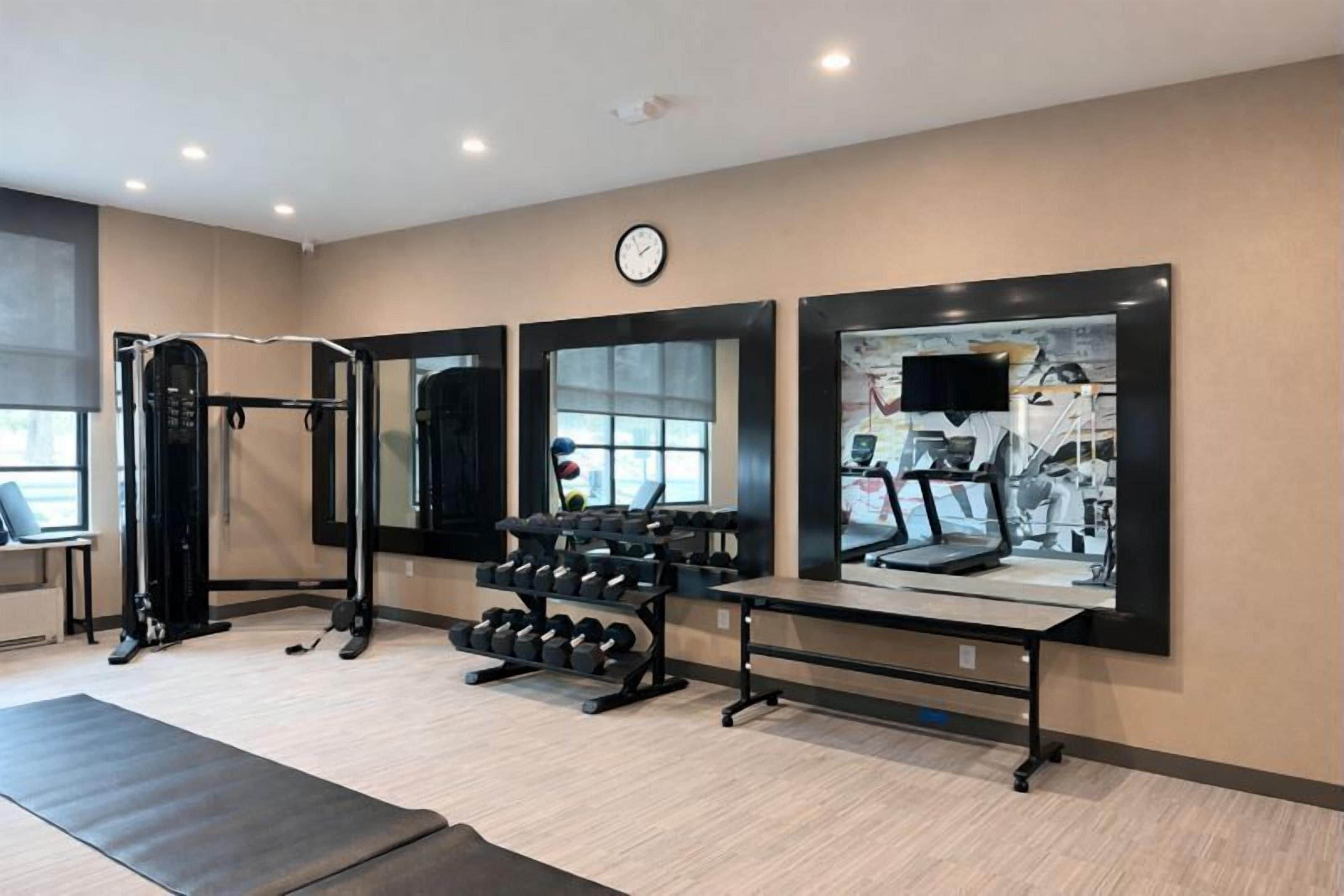 Un gimnasio con equipo de ejercicio, espejos y un reloj en la pared.