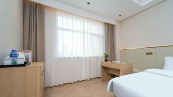A hotel room with a bed, a desk, a chair, a window with curtains, a bedside table with a lamp, and a water dispenser.