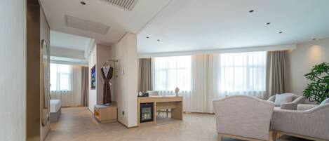 A spacious living area with a sofa, a coffee table, and a TV. There is a robe hanging on a rack and a small table with a lamp.