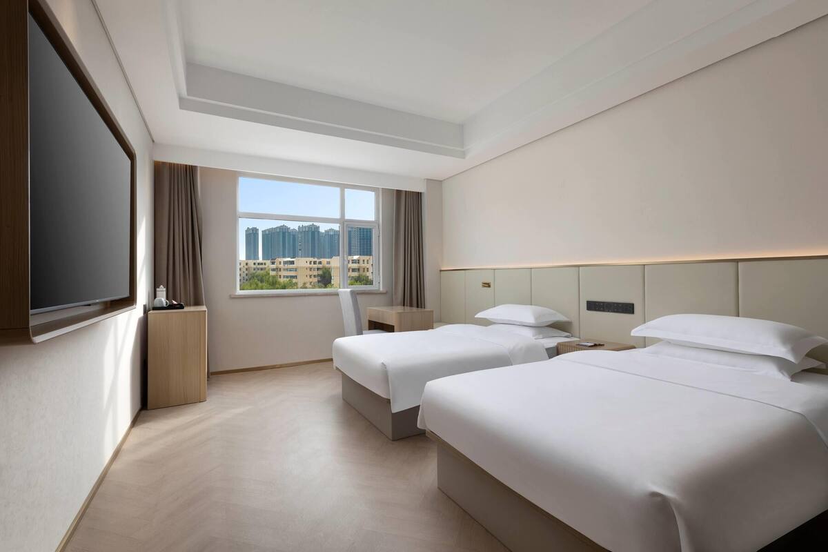 Camera d'albergo con due letti, TV, finestra vista città e arredamento moderno.