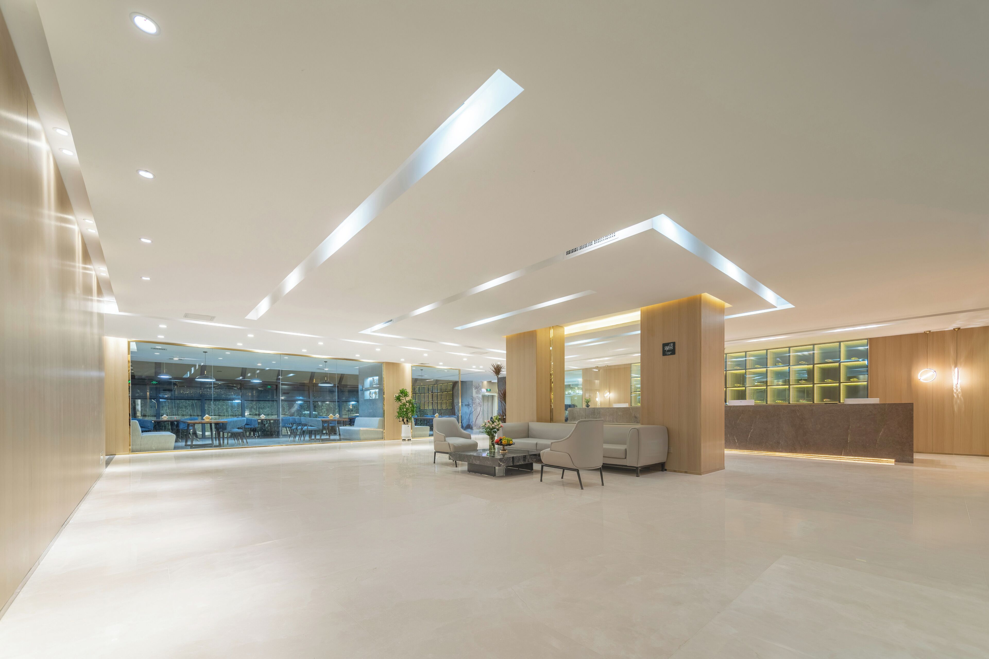 A spacious lobby with a reception desk, seating area, and a glass wall offering a view into the dining area.