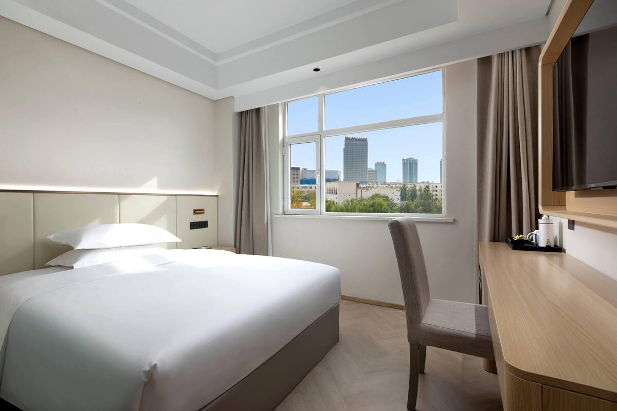 Camera d'albergo con un ampio letto, una scrivania e una finestra vista città.