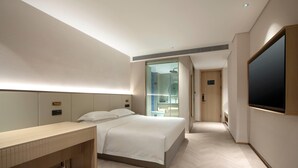 Ett modernt hotellrum med en säng, ett sängbord och en stor, platt-TV som är monterad på väggen.