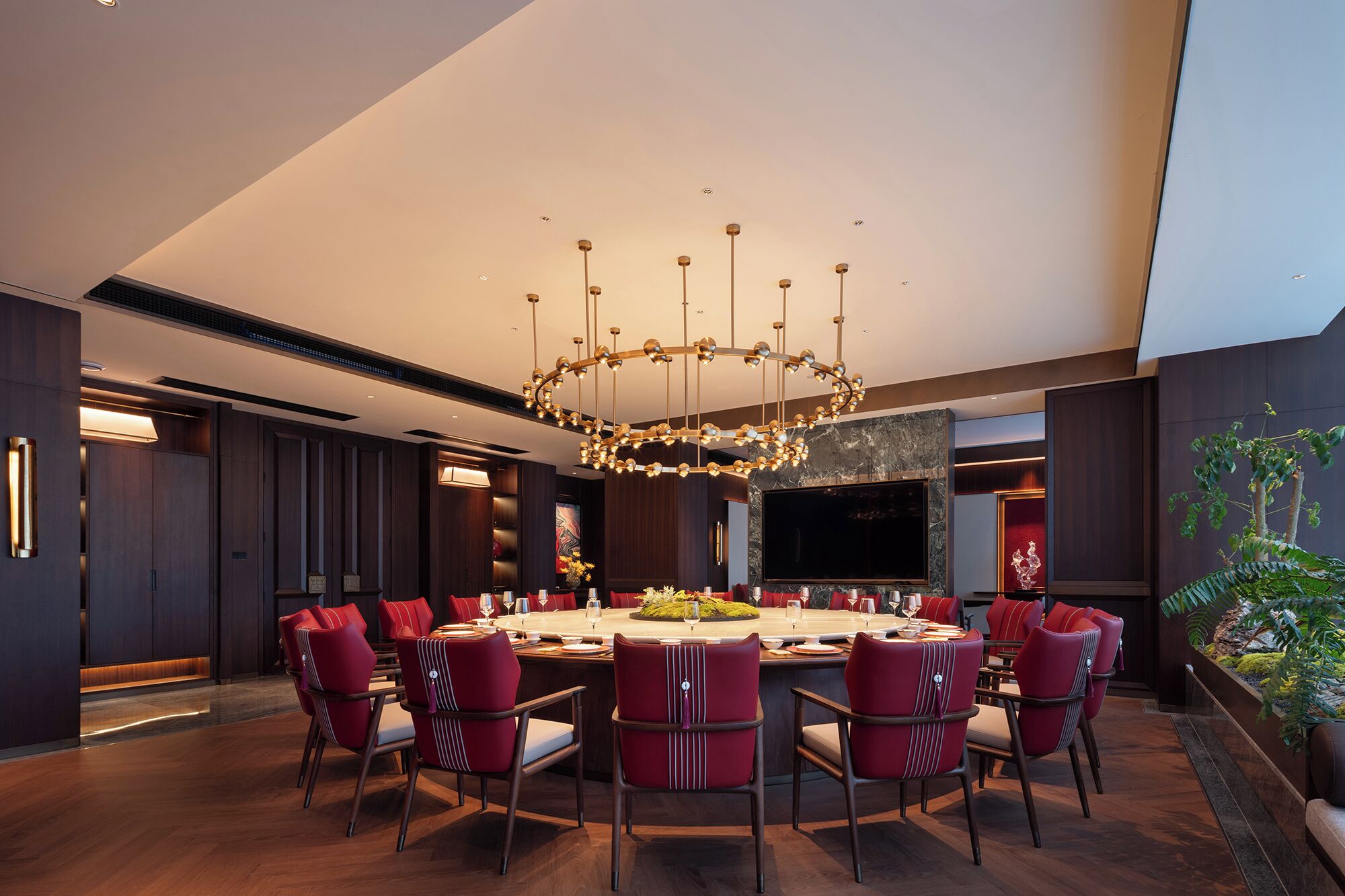 A modern dining area with a round table, red upholstered chairs, and a unique chandelier.