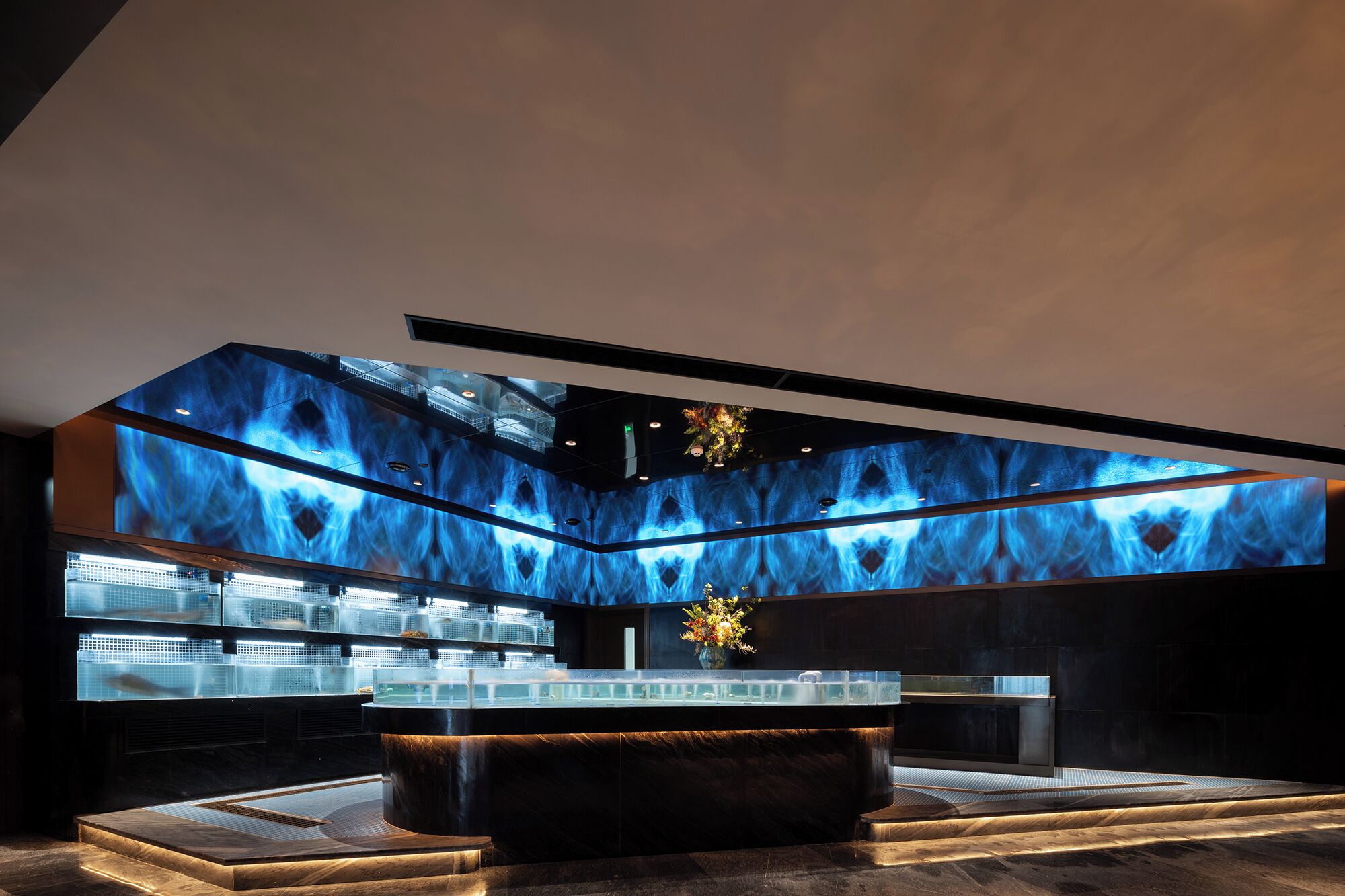 A modern interior with a central bar area, a ceiling with a blue light pattern, and a view of the cityscape through large windows.